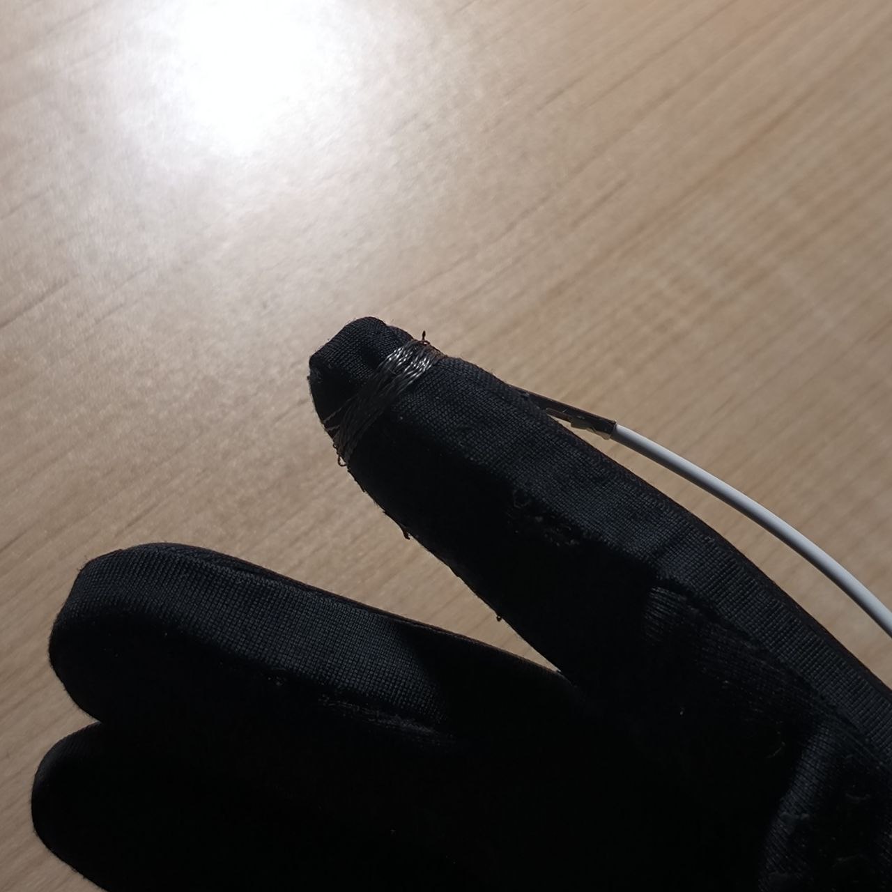 A conductive wire is sewn or taped onto the tip of a glove finger, creating a wearable key. This setup allows the user to interact with copper tape on a paper interface without bare skin contact—an important step toward building a wearable controller.