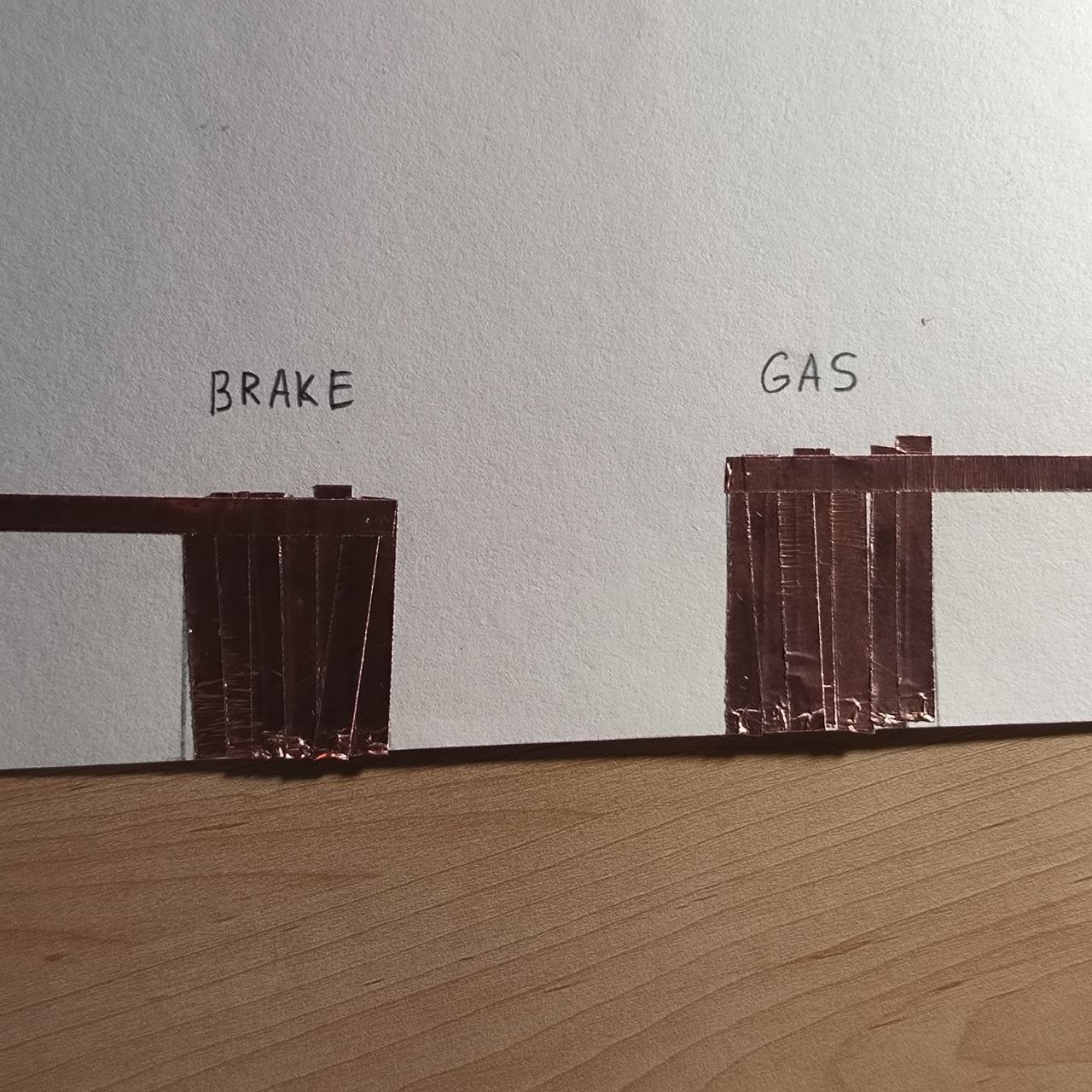 Copper tape is now fully applied to the paper to form the two distinct conductive pads for “BRAKE” and “GAS.” These will detect pressure or contact when the slipper touches them, functioning as digital foot pedals.