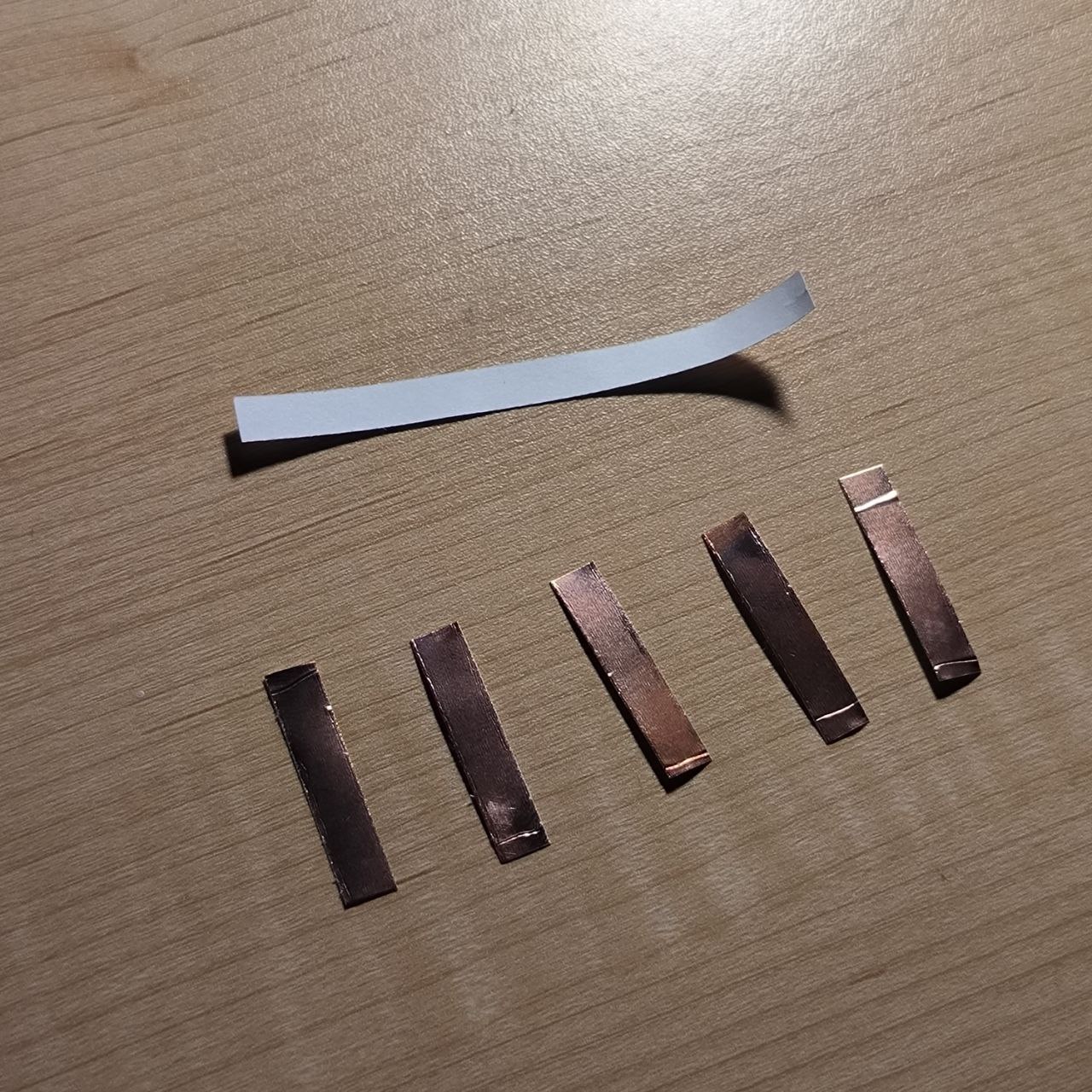 Strips of copper tape are neatly cut and ready for layout. These will be used as touch-sensitive inputs that respond to finger contact. A white backing strip suggests potential insulation or structure support.

      