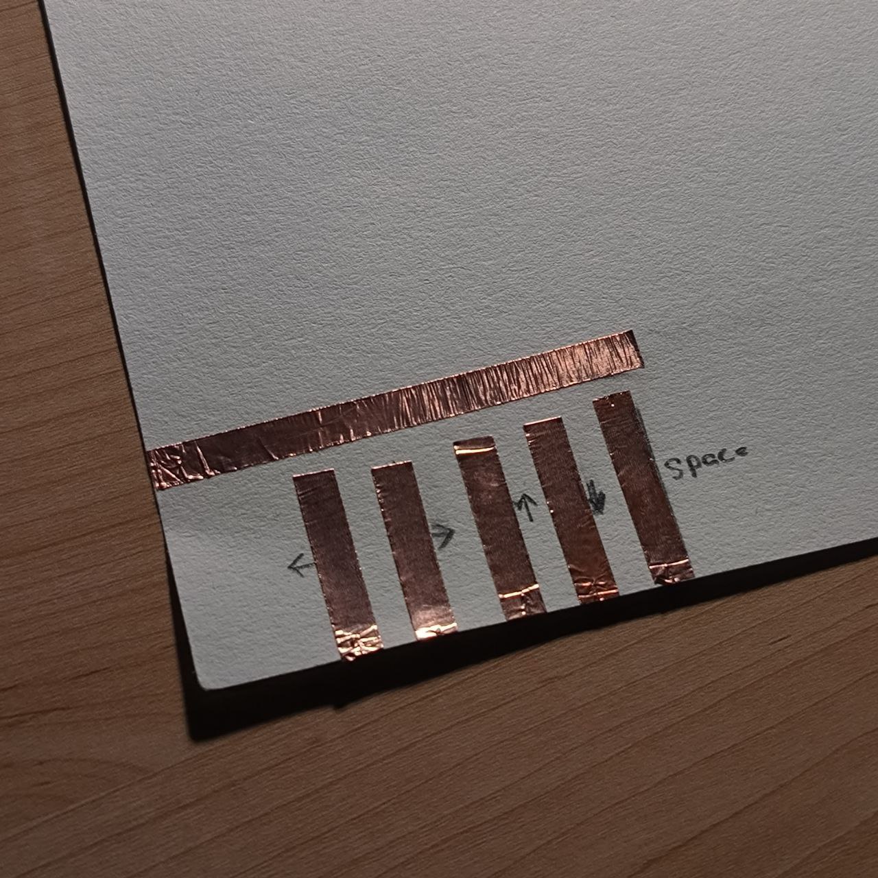 The copper strips are applied vertically to the paper and labeled with directional controls (left, right, etc.) and “space.” This layout mirrors a simplified keyboard, transforming the page into an interactive surface.

      